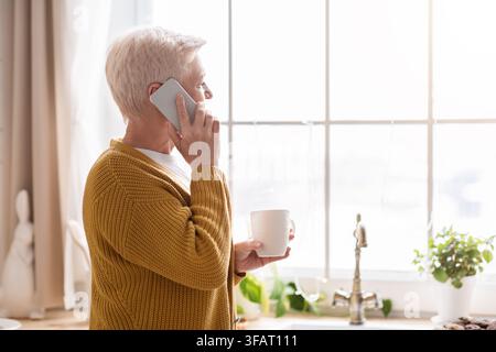 Side view of old lady talking on phone in kitchen Stock Photo