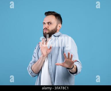 Repulsed millennial guy rejecting something, making STOP gesture over blue studio background Stock Photo