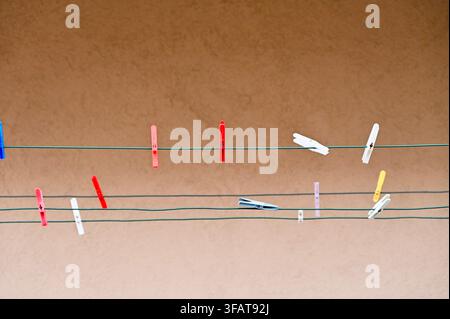 A horizontal studio photograph featuring an artistic composition of various colorful plastic clothespins attached to parallel wire lines against a solid textured brown background. Stock Photo