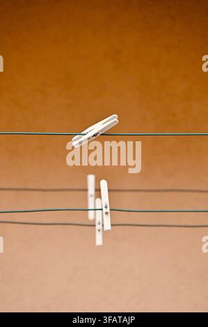 A photograph showcasing an artistic composition of white plastic clothespins attached to parallel wire lines against a solid textured brown background with negative space. Stock Photo