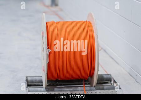 Large wooden spool loaded with orange telecommunication cable positioned on a metal roller dispenser during utility installation work Stock Photo