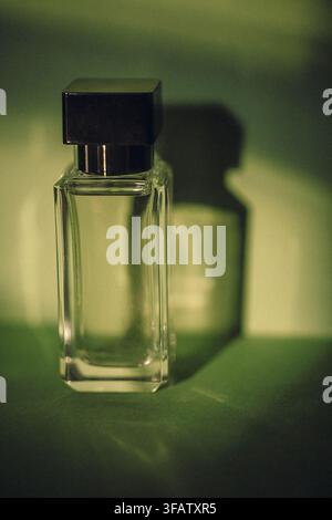 Clear glass bottle for perfume with a black cap, positioned against a green background, creating a soft shadow effect and highlighting its sleek desig Stock Photo