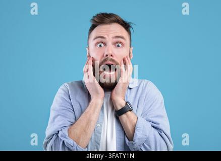 Scared young guy screaming in panic over blue studio background Stock Photo