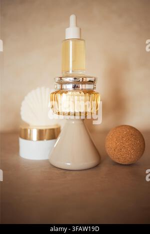 Stack of various cosmetic containers including a glass dropper bottle and cream jar with a decorative cork ball on a neutral background Stock Photo