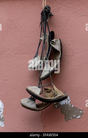 A bunch of shoes hanging from a wall. The shoes are old and worn, and they are hanging upside down. The scene gives off a sense of nostalgia and a fee Stock Photo