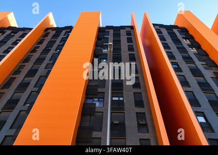 Low-angle view of a modern high-rise building with dramatic orange vertical fins alternating with dark brick facade sections, rising against a clear b Stock Photo