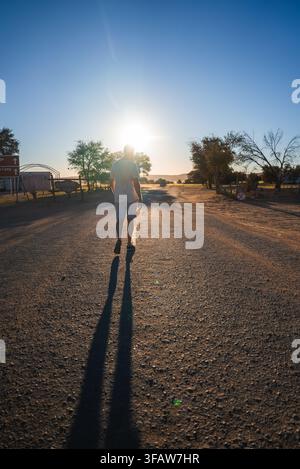 A man walks along a dirt road toward the sunset in Namibia Stock Photo