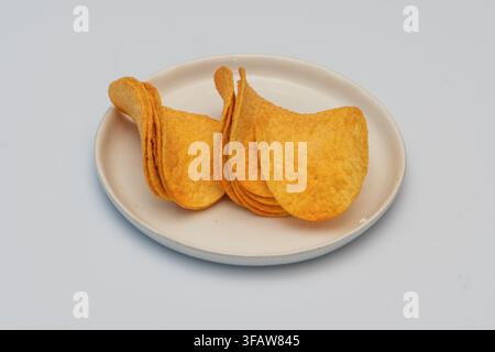 A small stack of potato chips sits on a plate against a white background. Stock Photo