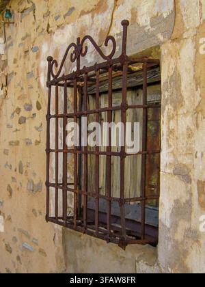 Rustic old window bars protecting a weathered wooden window on a stone wall Stock Photo