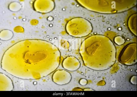 A macro photograph featuring vibrant yellow drops and pools of olive oil suspended and floating in clear water, creating an abstract scientific pattern with soft refractions and fluid dynamics. Stock Photo