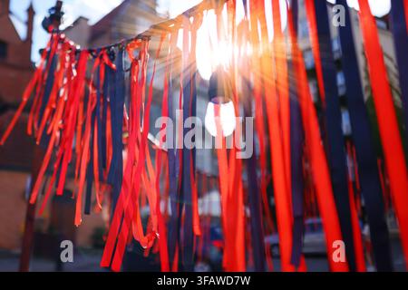 Decorative red and black ribbons illuminated by sunlight on a city street, abstract festive background with selective focus. Stock Photo