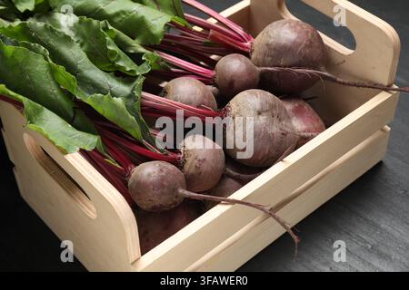 Many young beets with green leaves in wooden crate on dark textured table, closeup Stock Photo