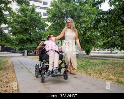 Woman assisting a man using an electric wheelchair in a city park Stock Photo