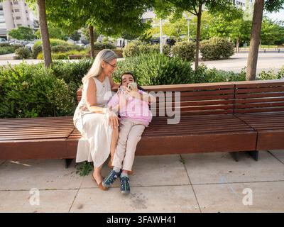 Mother and son with intellectual disability happily video calling on a park bench Stock Photo