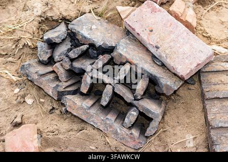 Broken industrial chimney liner segments and red bricks scattered on sandy ground surface, debris from demolished construction site showing textured w Stock Photo