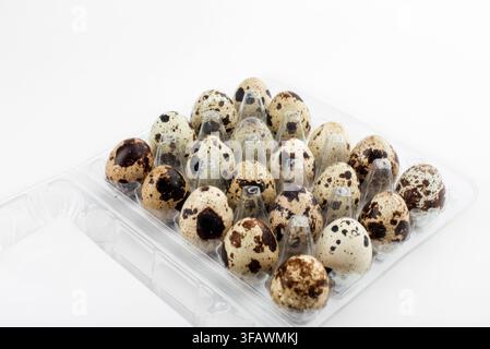 Many speckled quail eggs piled together in a clear plastic container package on a white background, organic farm product. Stock Photo