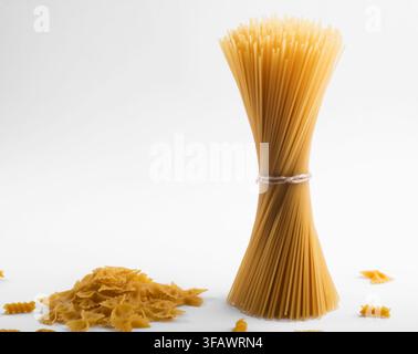 Raw spaghetti pasta tied in a bundle with scattered farfalle on a white background, Italian food and cooking concept. Stock Photo