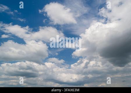 Scenic view of soft white cumulus clouds spreading across a vibrant blue sky during a clear daylight afternoon, ideal for nature background. Stock Photo