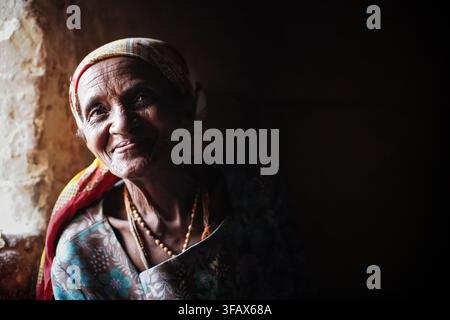 Ivato, Madagascar - April 26, 2019: Local elderly Malagasy woman posing in her house next to window, closeup portrait. People here are poor but cheerf Stock Photo