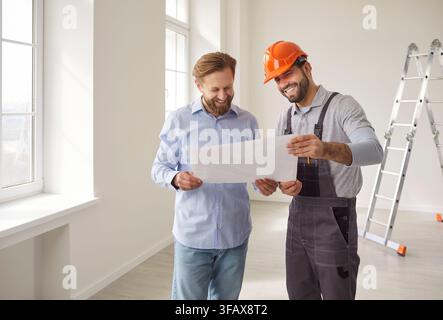 Foreman builder showing renovation plan to man client, posing in empty room with white walls Stock Photo