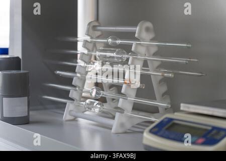 Volumetric glass pipettes resting on a white plastic rack in a chemistry laboratory with a digital balance nearby. Stock Photo