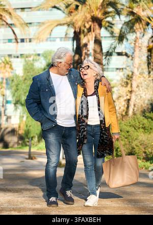 Affectionate senior couple walking arm in arm through sunny city park Stock Photo