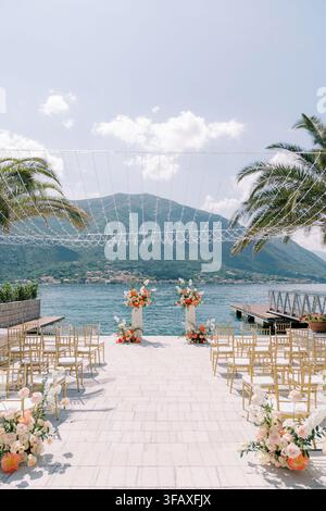 Elegant seaside wedding ceremony setup with chairs, floral arrangements, and mountain view Stock Photo
