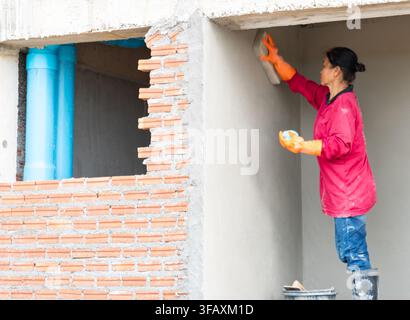 Female plasterer applying and finishing cement wall render at a modern building construction project. Stock Photo