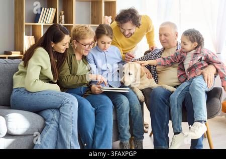Grandparents parents and kids using a tablet together at home with dog on sofa Stock Photo