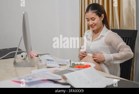 Pregnant woman working while monitoring financial data on computer screen gently holding belly have fruit Stock Photo