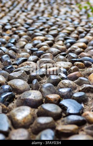 Traditional Italian pebble mosaic pavement, consisting of smooth, rounded river pebbles in shades of dark gray, glossy black, and earthy brown. Stock Photo