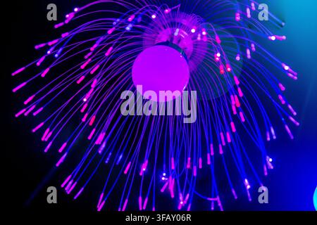 An illuminated decorative light fixture resembling a jellyfish, featuring a central glowing purple bulb surrounded by spreading fiber optic strands th Stock Photo