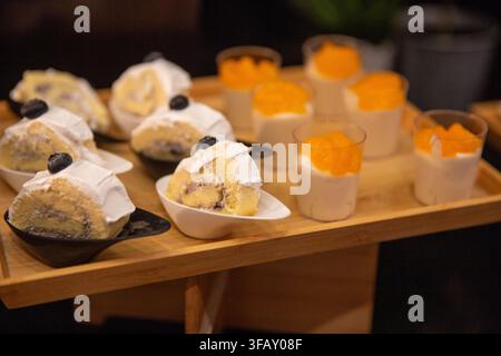 A gourmet dessert selection featuring individual slices of blueberry Swiss roll cake with white frosting and fresh blueberries, paired alongside small Stock Photo