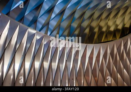 Abstract metallic interior ceiling with repeating folded panels in silver, gold and blue, modern architectural pattern. Stock Photo