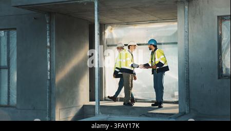 Shaking hands, team and construction workers at worksite for partnership, collaboration and agreement. Building development, civil engineering and Stock Photo