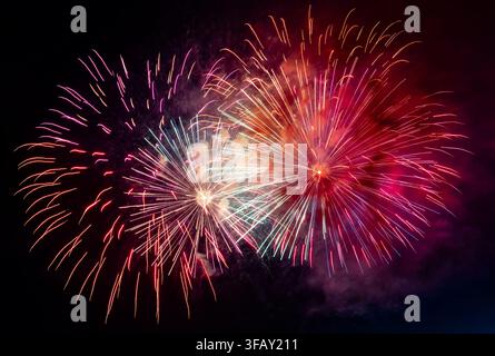 Colorful fireworks bursting in a dark night sky with vivid red, pink, purple, and white explosions creating a festive, celebratory atmosphere. Stock Photo