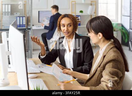 Diverse businesswomen discussing financial report at computer in office meeting Stock Photo