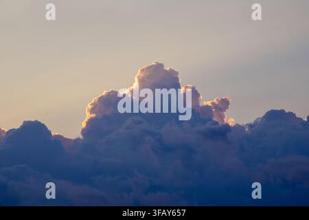 Large dramatic cumulus clouds illuminated from behind by warm sunset light, creating glowing golden edges above deep blue cloud layers. Atmospheric we Stock Photo