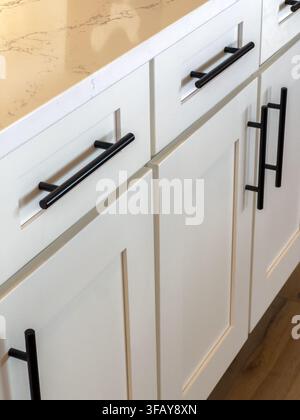 White kitchen cabinetry is shown with elongated black hardware handles. The composition focuses on the clean lines and contrast between light surfaces Stock Photo