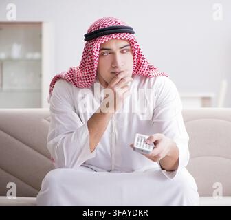 The young Arab man is watching TV and sitting on the sofa Stock Photo