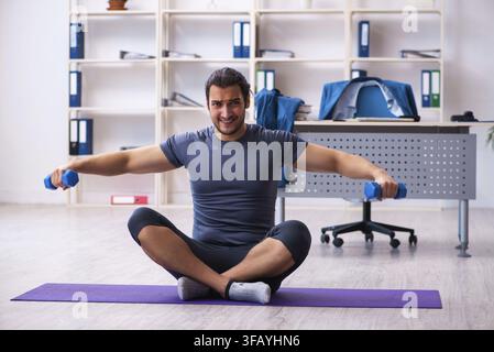 Young male employee doing sports exercises in office Stock Photo