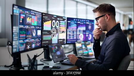 Young Data Analyst Using Laptop And Tablet To Track Financial KPIs. Stock Photo