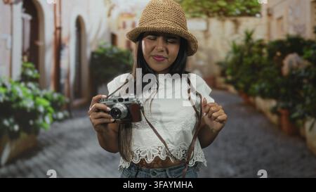 Woman adjusts vintage camera strap on a cobblestone street while squinting at the viewfinder; travel exploration frustration. Stock Photo