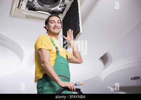 The young mechanic repairs the ceiling air conditioner Stock Photo