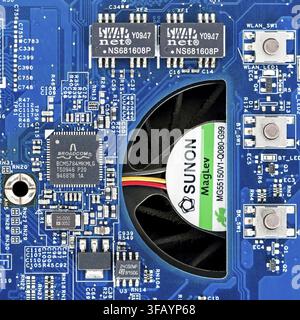 Close up of an Acer Aspire 5542 motherboard featuring the Broadcom BCM5784MKMLG Gigabit Ethernet controller chip beside a Sunon cooling fan on a blue Stock Photo