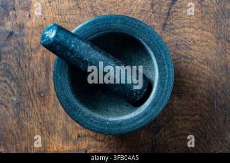Granite mortar and pestle on rustic wooden background, top view, close up. High angle view of heavy stone mortar with pestle placed on textured dark w Stock Photo
