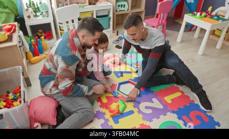 Man and boy placing wooden block into hexagon puzzle on foam number mat in a building playroom; playful bonding. Stock Photo