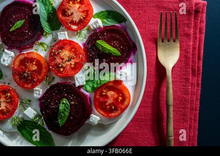 Gourmet beetroot and tomato salad, close up. Beautiful flat lay of fresh summer salad with sliced red beets, tomatoes, feta cheese cubes, and mint on Stock Photo