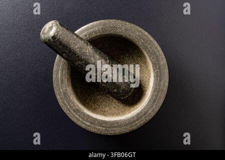 Granite mortar and pestle top view on black background, close up. Traditional stone mortar and pestle made of dark granite on black textured surface, Stock Photo