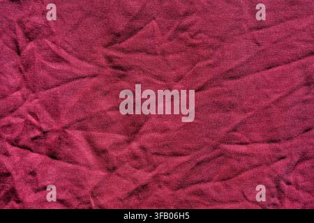 Crumpled burgundy fabric texture abstract background. Close up of wrinkled dark red cotton cloth with multiple creases, creating a detailed textured b Stock Photo
